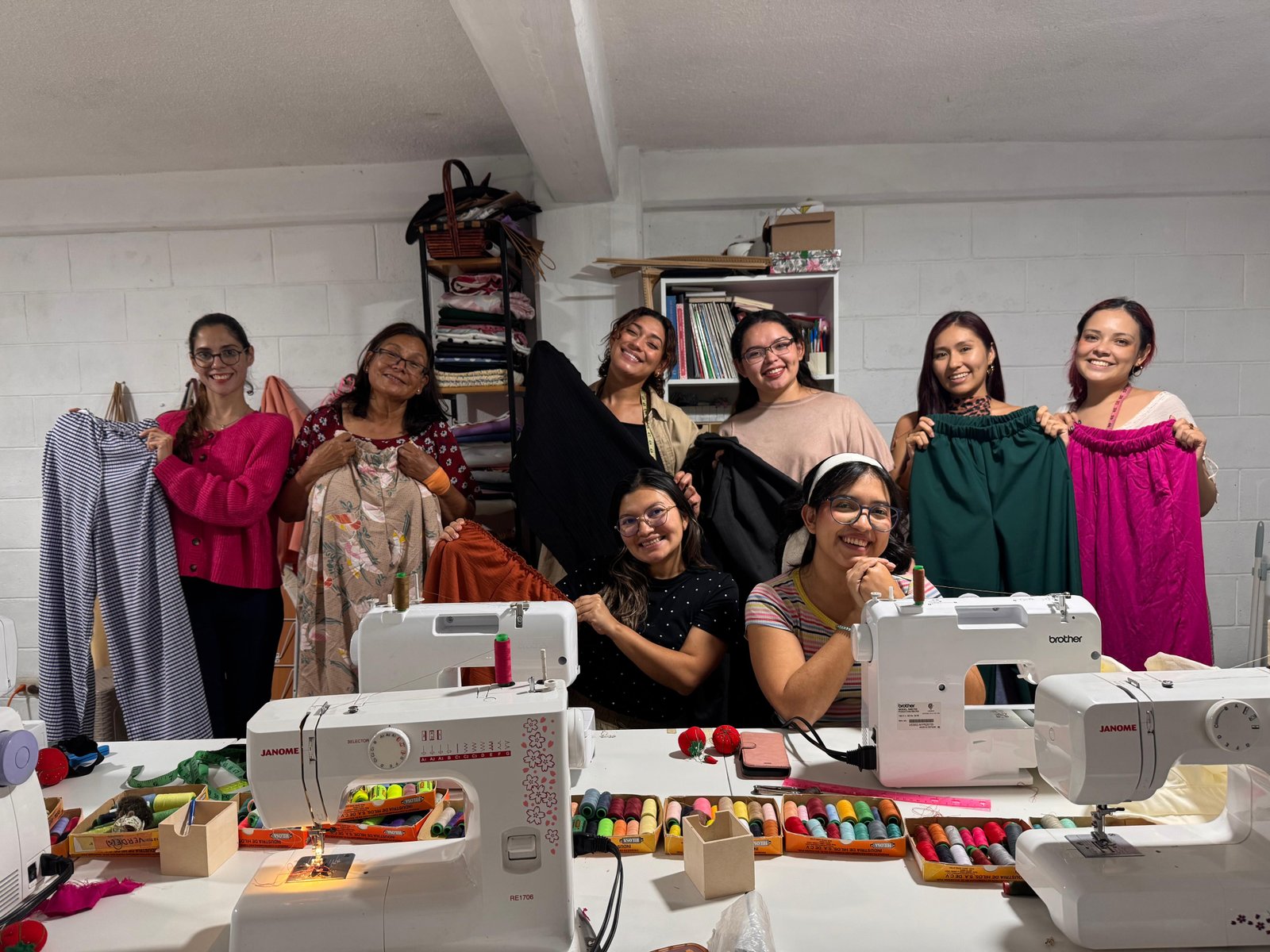 Grupo del taller de GALO Atelier mostrando prendas junto a las máquinas de coser
