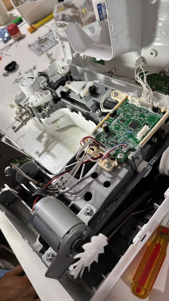Placa electrónica y motor de una máquina de coser abierta para reparación en GALO Atelier, El Salvador